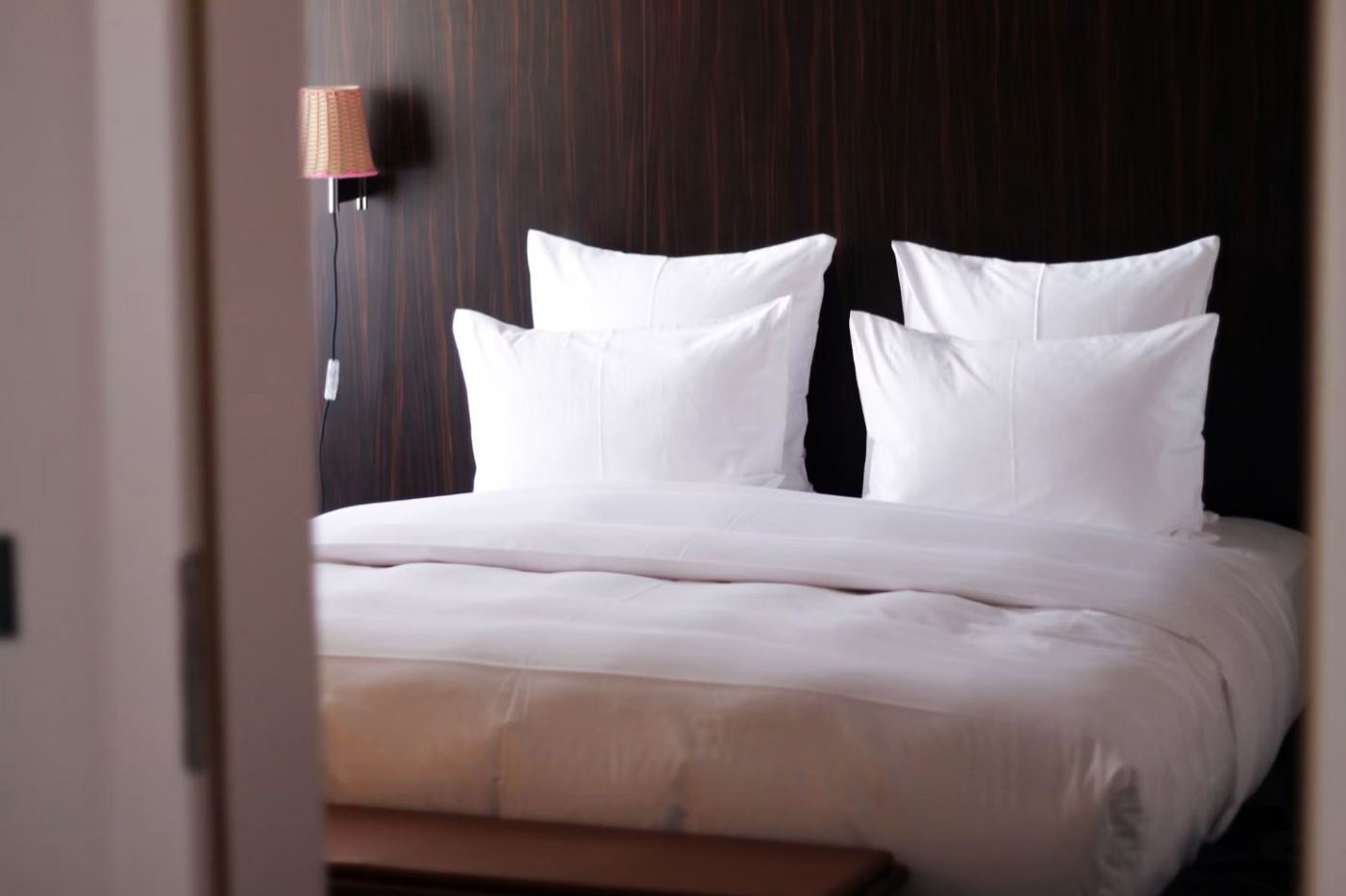 Lit d'hôtel avec quatre oreillers blancs devant une tête de lit en bois sombre